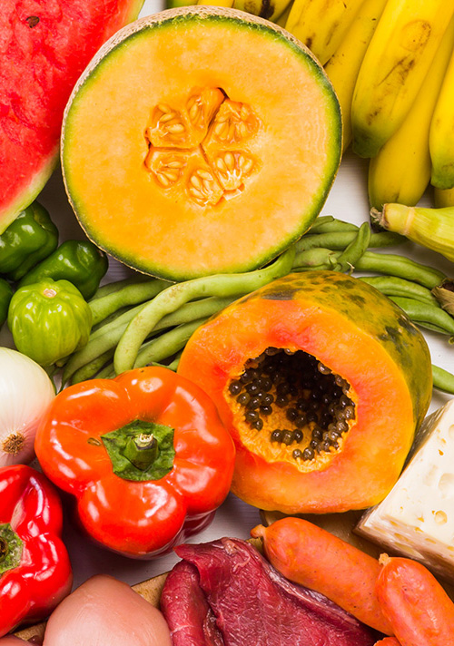 Variety of food including green and red bell peppers, onion, cantaloupe, bananas, green beans, papaya, sausages, red meat, and chicken.