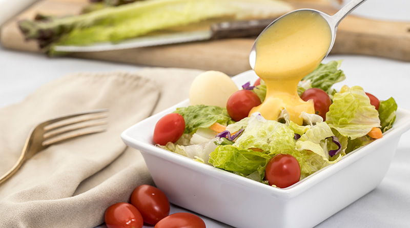 Colorful salad with a spoonful of dressing being poured onto it