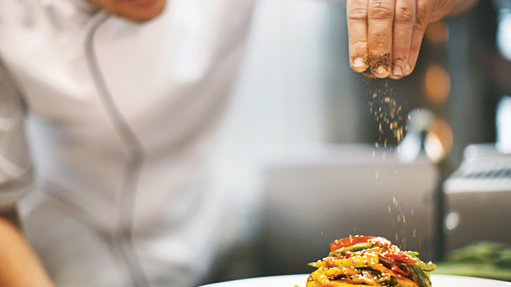 Chef sprinkling spices on a dish.