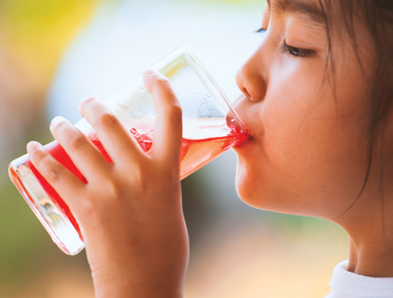child girl drinking red juice water with ice from glass