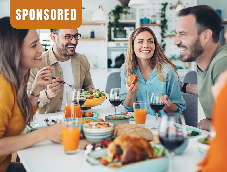 Group of friends sitting around a table at home, eating, drinking and talking