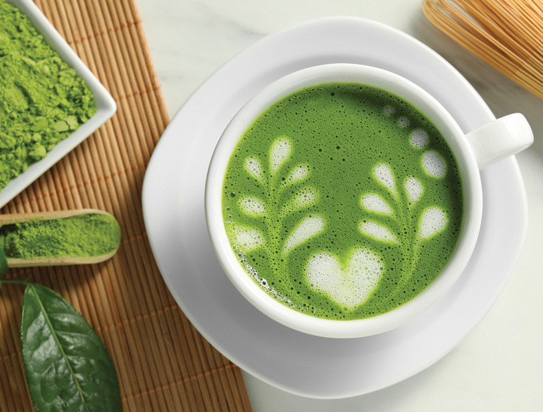 Delicious matcha latte, powder, leaf and whisk on white table