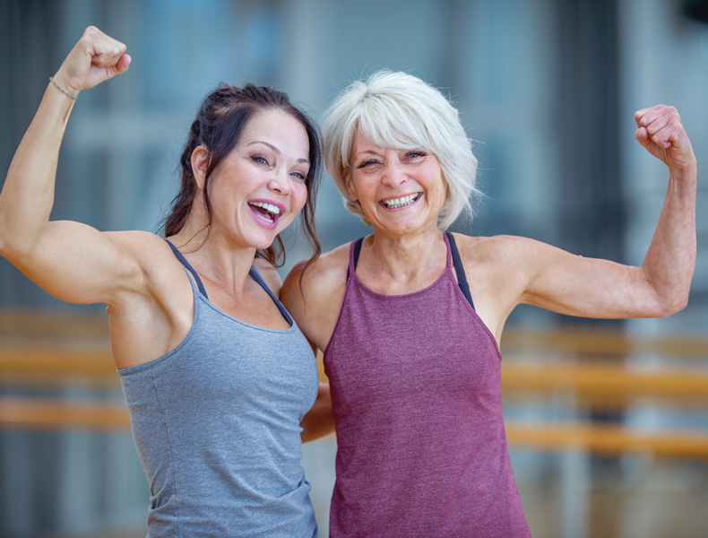 Two woman are seen posing together for a portrait in a fitness gym