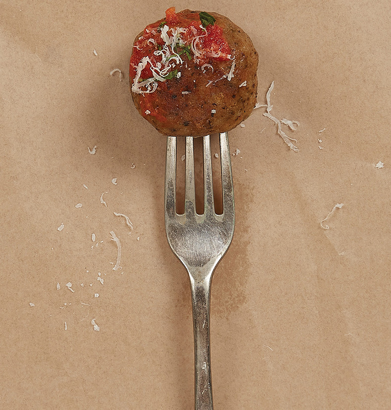 Fork through an Ivy Farm meatball with grated cheese, greens, and tomato on top