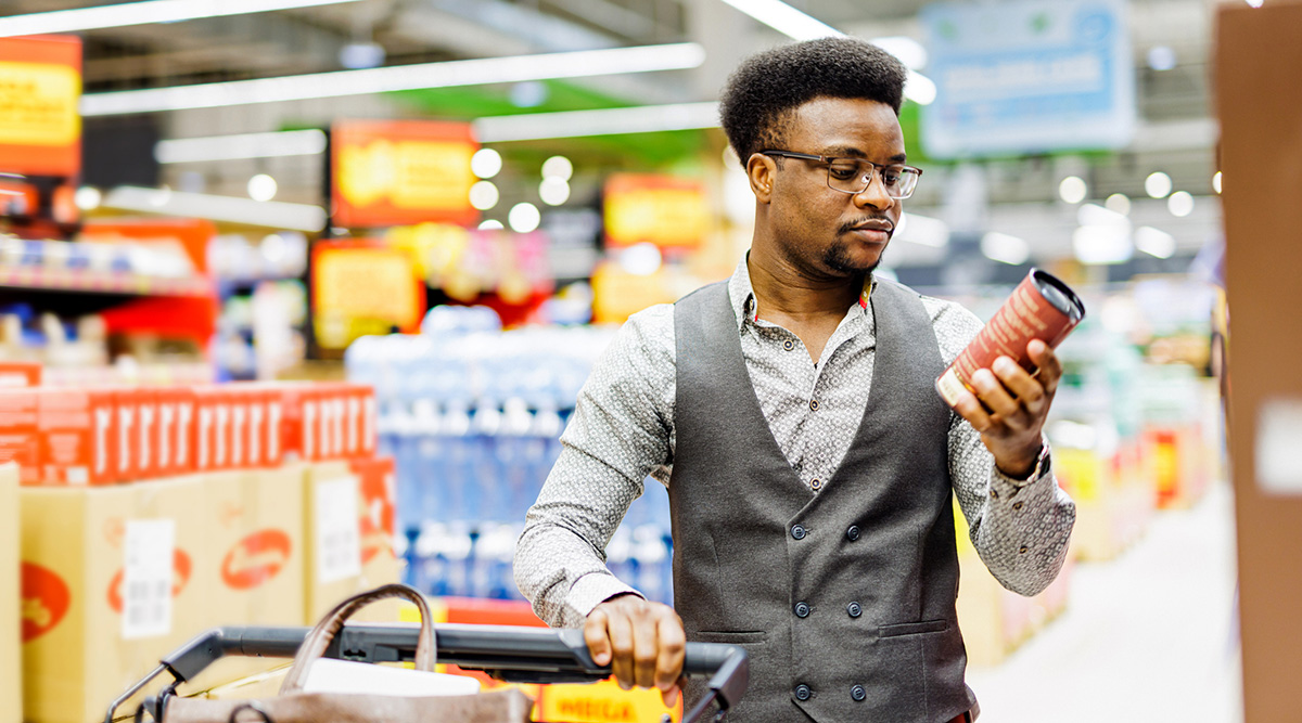 A man with a cart looking at a product at the grocery store.