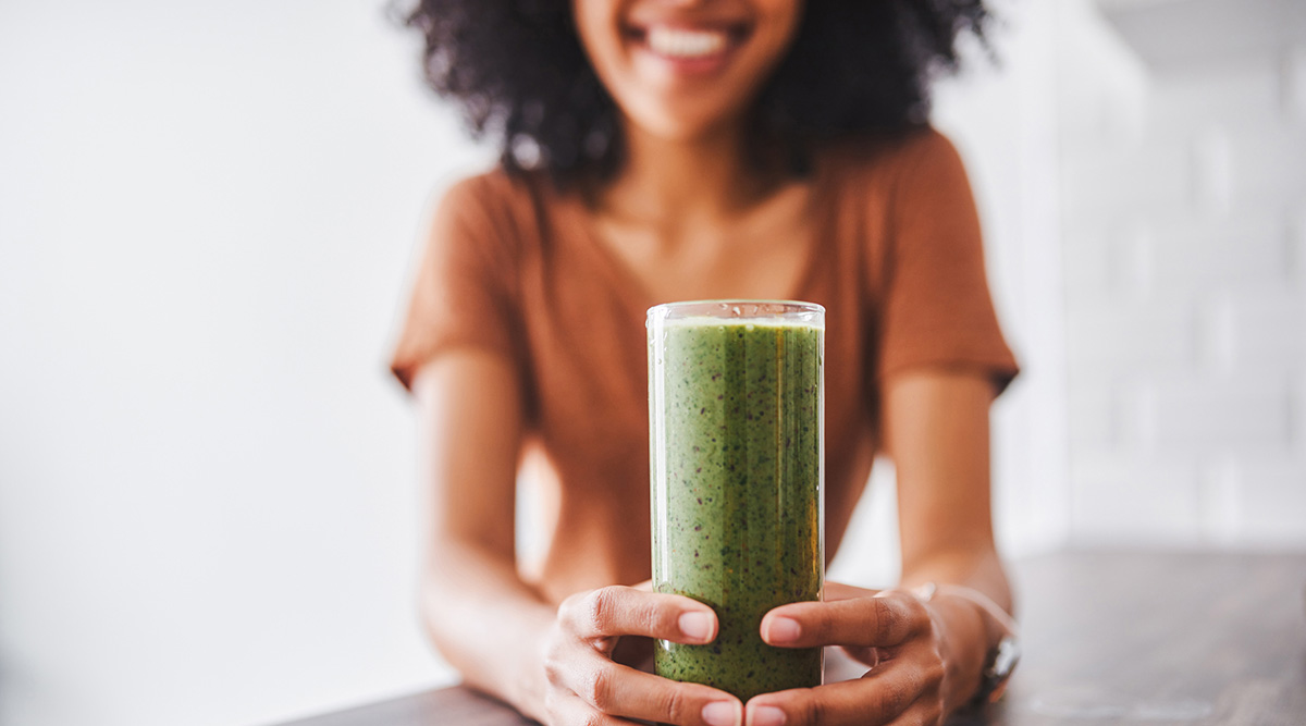 Woman smiling holding a glass of a green smoothie.