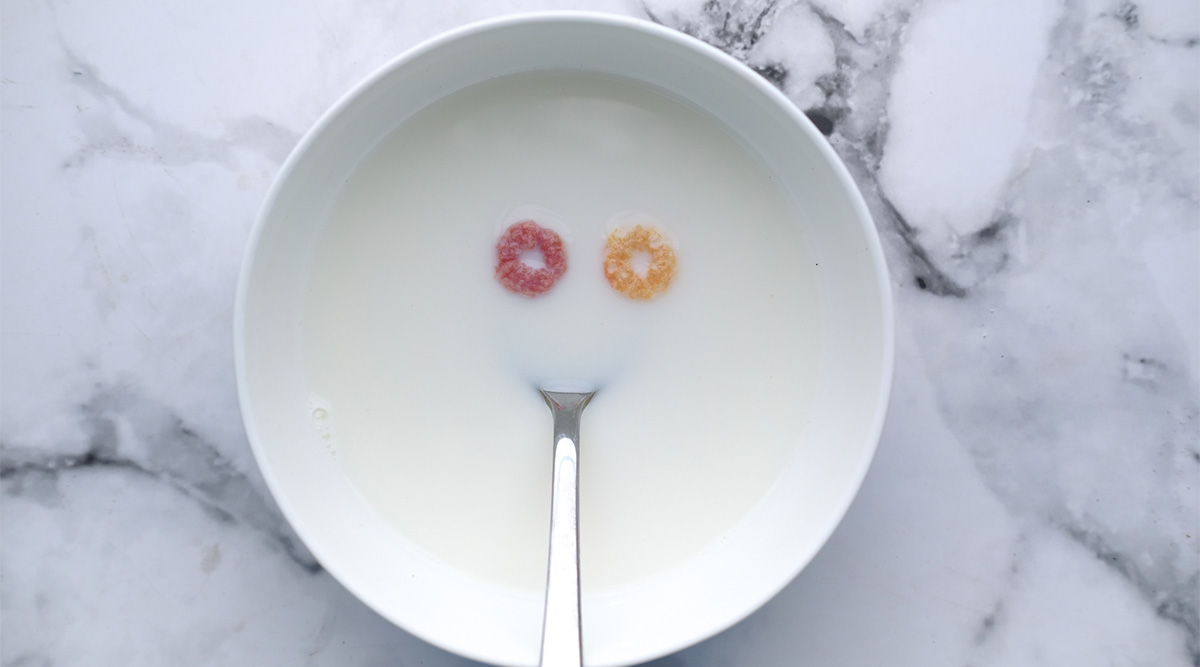 A bowl of milk with two pieces of cereal and a silver spoon.